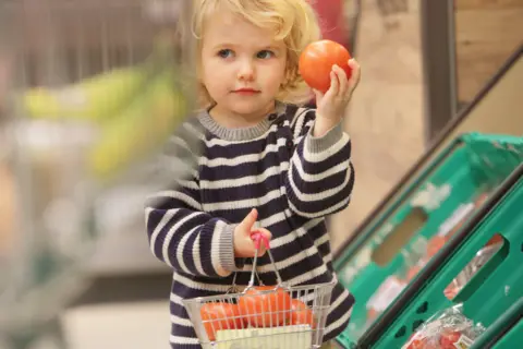 Getty Images Young child holds apple in supermarket