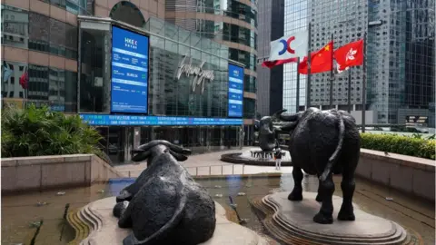 Getty Images Flags flutter next to the Hong Kong stock exchange, surrounded by glass-fronted skyscrapers.