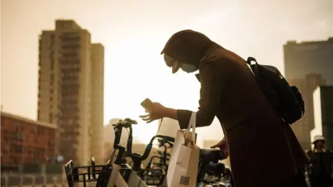 Woman in China wears mask and hood against backdrop of yellow sky