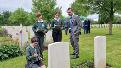 BBC/Naj Modak Children writing memories in front of war graves