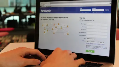 A person using a laptop. Facebook is displaying on the screen