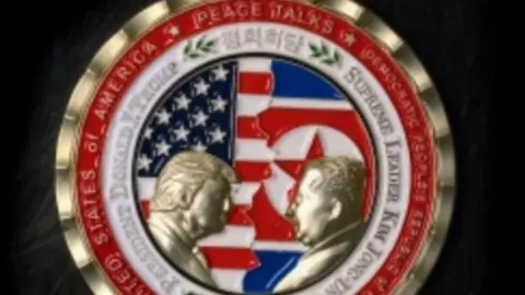 AFP A commemorative coin issued by the White House, depicting Mr Trump and Mr Kim facing each other in front of a background of US and North Korean flags. The words "Peace Talks" are emblazoned at the top of the front of the coin with the date "2018" beneath.