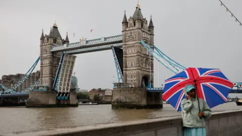Getty Images A man with a Union flag umbrella stands beside the stuck Tower Bridge