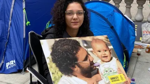 BBC Sanaa Seif holds a photo of her brother Alaa Abdel Fattah and his son at a sit-in protest outside the Foreign, Commonwealth and Development Office in London, UK (1 November 2022)