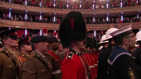 BBC Poppies fell from the ceiling over members of the Royal Navy, the Army and Royal Air Force who stood in the centre of the hall