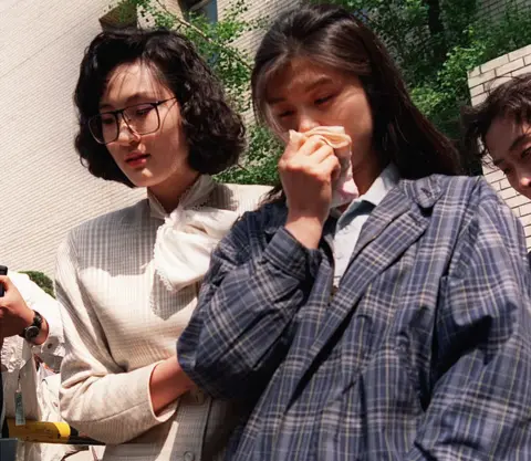 AFP via Getty Images Kim Hyun-hui holds a handkerchief to her nose as she is led from a courtroom in Seoul by a woman investigator, on 25 April 1989