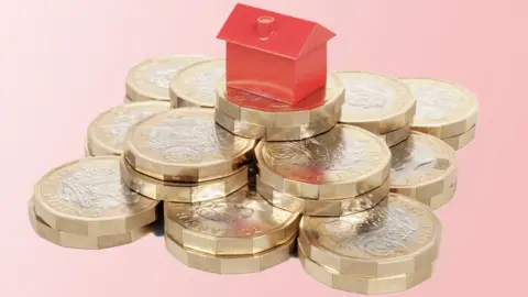 Getty Images Miniature red house resting on a pile of pound coins.