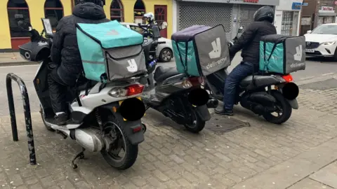 Marc Atkins/Getty Images Deliveroo drivers parked on pavement