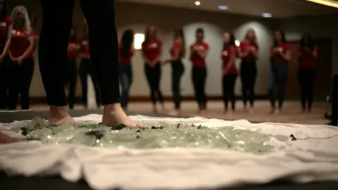 Contestants walk over glass during an empowerment workshop