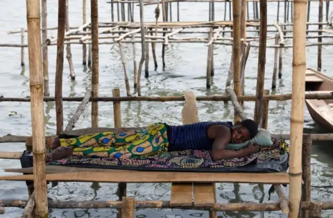 Reuters A man sleeps on wooden stilts built on a lagoon in the Makoko fishing community in Nigeria"s commercial capital Lagos February 26, 2022. Picture taken February 26, 2022.