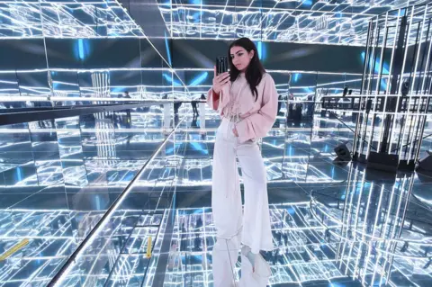 Tabatha Fireman/ Getty Images Charli XCX takes a photograph in a mirrored cube