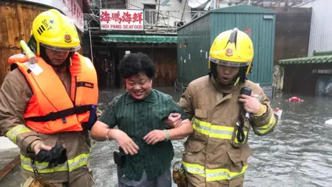 AFP Fire rescue workers rescue a woman in floodwaters in the village of Lei Yu Mun during Super Typhoon Mangkhut in Hong Kong on 16 September 2018.