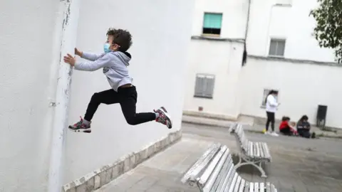 Reuters Kilian, 6, wears a protective face mask as he jumps from a bench, after restrictions were partially lifted for children, during the coronavirus disease (COVID-19) outbreak, in Igualada, Spain, on 26 April 2020