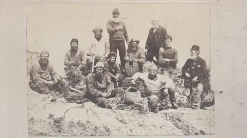 Jersey Heritage Photograph taken at the Écréhous. Ouless is stood on the backrow with his hand on someone’s shoulder