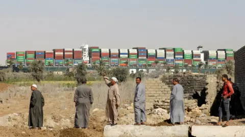 Reuters Onlookers watch as a container ship stuck for days in the Suez Canal resumes its travel