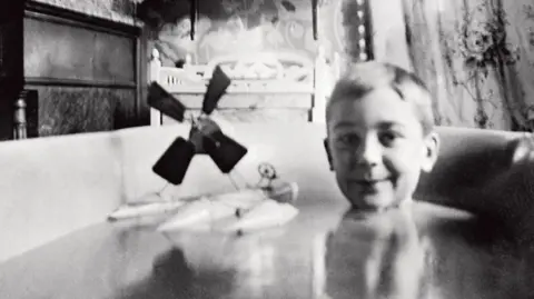 Jacques Henri Lartigue sits in a bath with a toy plane