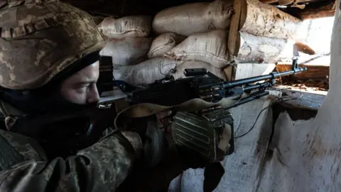 Getty Images A Ukrainian serviceman points a machine gun through an opening in a sandbag bunker during military exercises