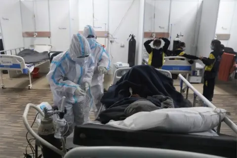 EPA Indian medical professionals wearing Personal Protective Equipment (PPE) attend to patients inside a Covid-19 care centre and isolation ward facility, in an indoor stadium inside Commonwealth Games (CWG) Village sports complex in New Delhi, India, 04 January 2022