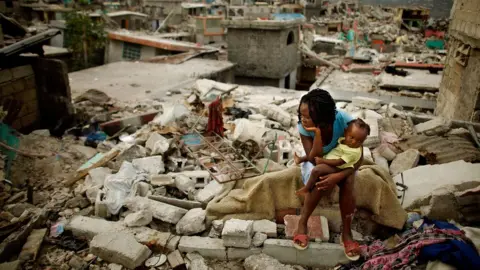 Getty Images A mother and her daughter sit on the spot where their home collapsed during the earthquake, February 26 2010 in Port-au-Prince, Haiti.