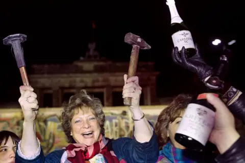 Getty Images A berliner holds up a hammer and a chisel early on November 15, 1989 in front of the wall at the Brandebourg Gate partly visible behind it as a crowd of people demonstrated for the destruction of the wall for a passage way between the East and the West near the monument.