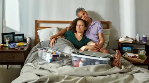 BBC Jennifer Brea and Omar Wasow in bed, surrounded by medication
