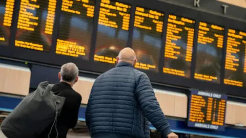 Getty Images Passengers looking at departure board