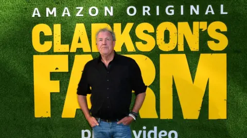 PA Media Clarkson in front of a poster for his show