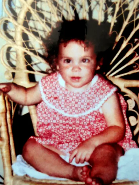 Family handout Katrice Lee, wearing a red-and-white dress, sitting on a chair