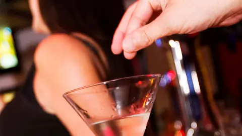 Alamy A person spikes a drink in a bar