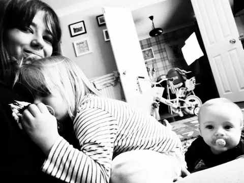 Ellie-Mai Holmes-McClure A black-and-white photo of a woman at home with two children