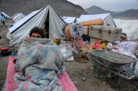 EPA An Afghan refugee has himself wrapped in a quilt against the cold at a tent camp after returning from neighbouring Pakistan, at the Afghanistan-Pakistan border in Toorkham, Afghanistan, 18 November 2023