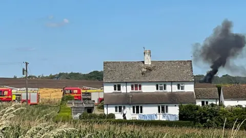 A house and two fire engines with smoke coming from field