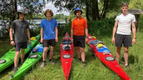 Maddie Rolfe Four males stood beside their kayaks on the grass