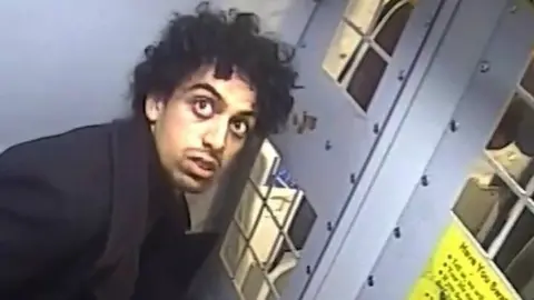 Louis De Zoysa in the cell at the back of the police van, looking at the van's CCTV camera