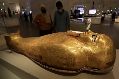 Reuters People look at a large gilded sarcophagus.