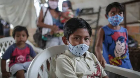 Getty Images Indigenous boys wearing protective masks wait for vaccine and testing at Parque das Tribos community, on May 21 2020 in Manaus