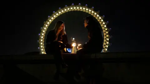 Getty Images A couple sit on a wall opposite the London Eye with candles on March 23, 2021 in London, England.