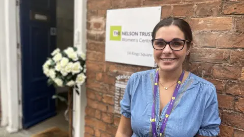 A woman in a denim dress outside the front door of a building