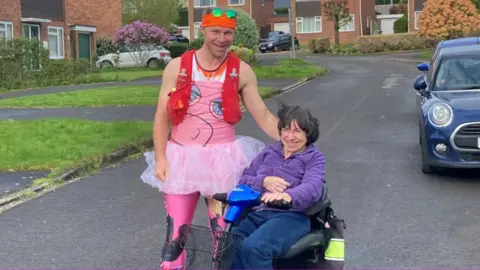 BBC Phil Wiseman on the street wearing a pink tutu and leggings, next to his mum who is in a motorised wheelchair