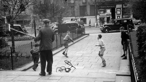 John Murray A man with a broom chases away a group of unruly boys from a Dundee park