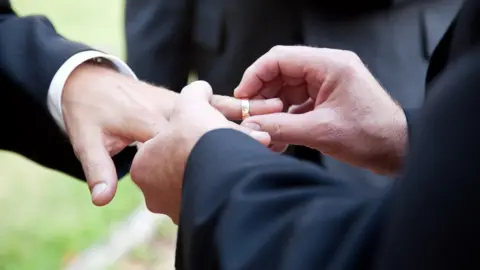 Getty Images/Lisafx Husbands exchanging wedding rings