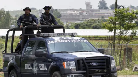 Getty Images A unit of the Mexican Federal Police patrols the surroundings of the Puente Grande State prison (background) in Zapotlanejo, Jalisco State, Mexico, on 9 August,