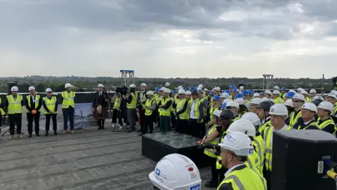 University Hospitals Dorset Scores of people wearing hi-viz vests and white hard hats at a topping-out ceremony