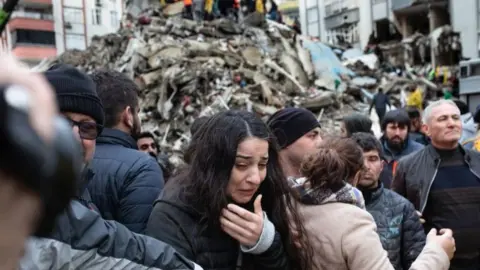 Getty Images A woman in tears with a mound of rubble behind her.