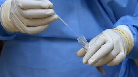 Reuters Medical staff wearing surgical clothes holds test tube