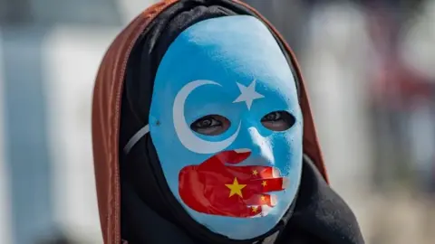 AFP/Getty A protester against China's actions in Xinjiang wears a mask with the colours of the flag of East Turkestan