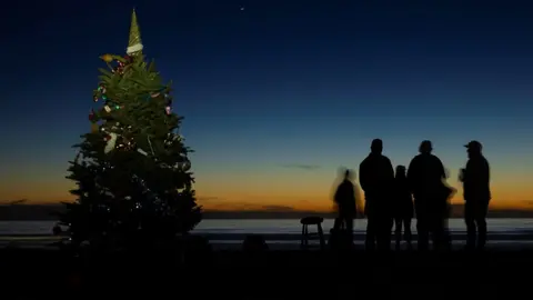 Mike Blake / Reuters Groups of people gather near a Christmas tree on the beach