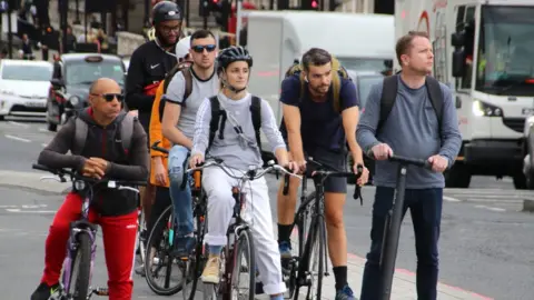 Getty Images Cyclists and an electric scooter rider wait at traffic lights near Westminster Bridge