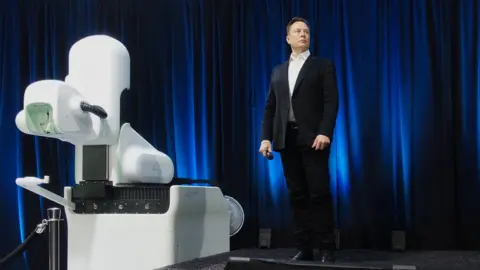 Steve Jurvetson Musk next to Neuralink R1 machine.