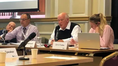 Martin Heath/BBC Councillors sitting at a desk. The middle one is wearing a black sleeveless sweater and white shirt.